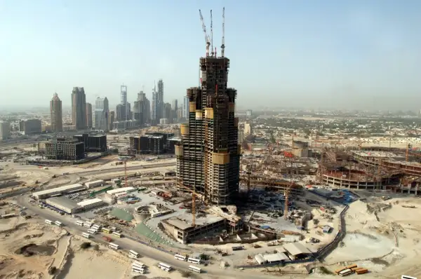Budowa Burj Khalifa w Dubaju, widok z lotu ptaka na plac budowy, dźwigi i inne wieżowce w tle.