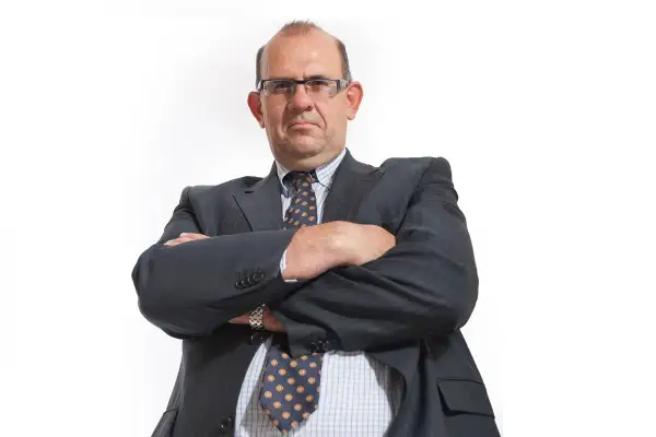 Mężczyzna w garniturze i okularach ze skrzyżowanymi rękami.