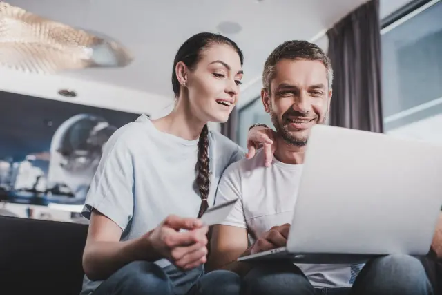 Para sprawdzająca dewelopera przed kupnem mieszkania, analizująca dane na laptopie i trzymająca kartę.